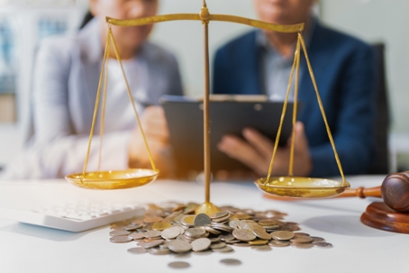 Legal scales sitting on top of coins symbolizing law firm revenue and profitability, with two professionals discussing finances.