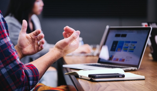 A man gestures while viewing a laptop, likely discussing website media.