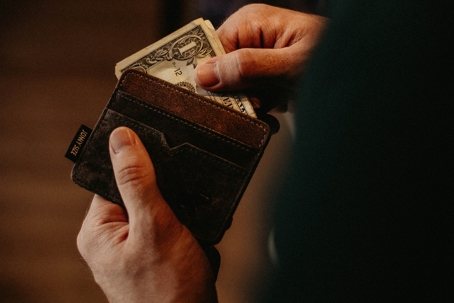A pair of hands holds a brown wallet with a dollar bill partially pulled out.