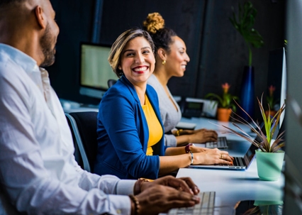 Diverse team members collaborate at their desks, smiling and working on computers.
